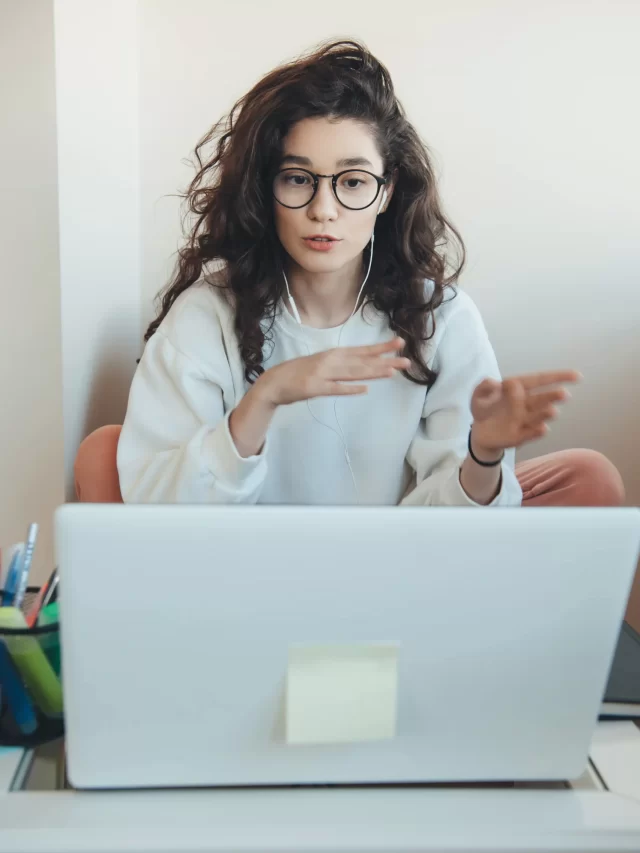 curly-haired-young-woman-with-glasses-is-explaining-something-laptop-online-meeting-from-home