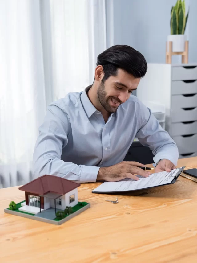 man-sits-desk-with-house-small-model-house